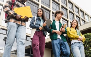 Four college students carrying notebooks are pictured smiling and laughing.