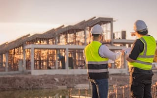 Construction workers in bright green vests and white hard hats standing at a job site are shown.