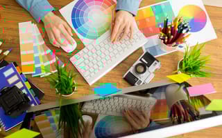 A graphic designer is depicted typing on a keyboard surrounded by color samples..
