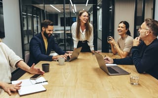 Five happy colleagues chat together while working on a project in an office conference room