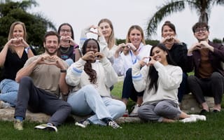 Several Calm team members pose for a group photo in an outdoor setting while creating heart symbols with their hands