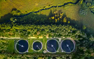 Aerial view of four large industrial tanks surrounded by lush green forest and grass.