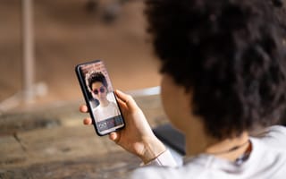 Delhi’s PointAI Raises ₹47 Crore in Pre-Series A Round A person holds a smartphone displaying a virtual try-on app, featuring them wearing augmented reality sunglasses. The setting is casual and modern.