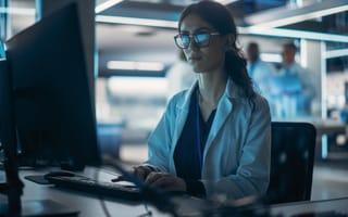 A scientist in a lab coat works at a computer station in a dimly lit, high-tech laboratory. The atmosphere conveys focus and innovation.