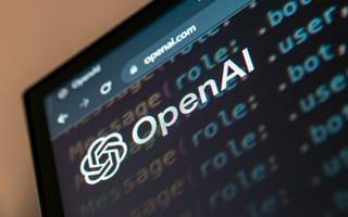 Close-up of a monitor displaying the OpenAI logo with code lines in the background. The screen shows a website URL, suggesting a tech-focused atmosphere.