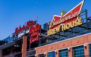10 Largest Companies in St. Louis to Know Red and gold signs for "Cardinal's Nation" and "Budweiser Brew House" against a clear blue sky, mounted on a brick building, conveying excitement.