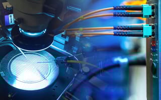 MetaOptics Establishes U.S. Subsidiary to Advance Semiconductor Optics Close-up of semiconductor manufacturing equipment under a microscope, with illuminated microchips and connected fiber optic cables, conveying precision.