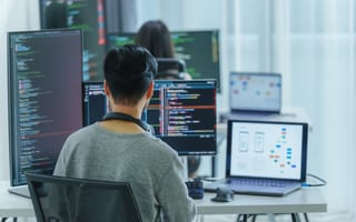 A person sits at a desk with multiple monitors displaying code and diagrams. The setting is a bright office environment, conveying a focused, tech-driven atmosphere.
