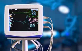 Medical monitor displaying heart rate and vital signs in a hospital setting. The screen shows numerical data and colorful graphs against a blurred background.