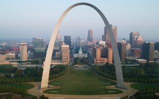 Aerial view of the iconic Gateway Arch towering over downtown St. Louis. The arch frames modern skyscrapers and green parkland, evoking a tranquil urban scene.