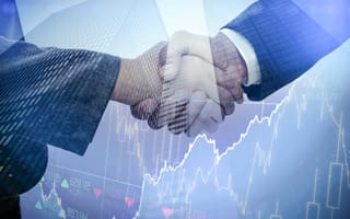 A handshake between two people in suits overlays skyscrapers and stock market graphs, symbolizing financial agreement and trust in business.