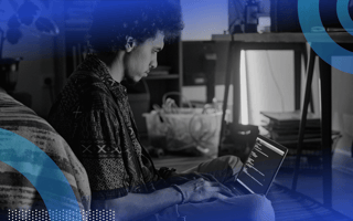 A developer works on a laptop next to a bed