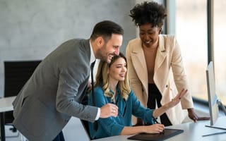 Three smiling colleagues view a project on a computer monitor screen while working together in an office