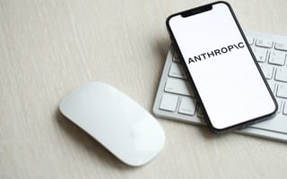 A mobile phone featuring the Anthropic logo sits on a computer keyboard next to a white computer mouse.
