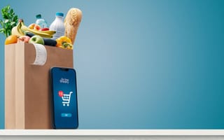 Grocery bag filled with goods is pictured with a smartphone propped up next to it.