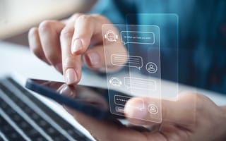 A close up of a pair of hands interacting with a mobile device with an illustration of messages with an AI chatbot hovering over the screen.