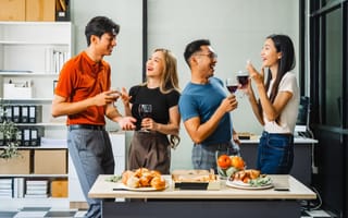 Four smiling colleagues chat together while enjoying wine and snacks in an office kitchen