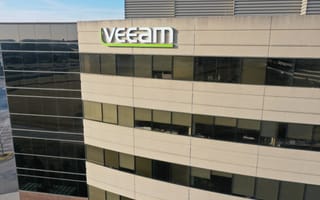 A modern office building with the "Veeam" logo in large letters. The facade has beige panels and reflective glass windows under a clear blue sky.