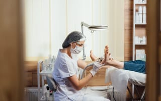 A podiatrist in protective gear, including mask and gloves, uses a tool for foot care on a patient in a treatment room with a calm atmosphere.
