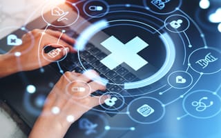 Hands typing on a laptop with medical icons and a glowing cross overlay. Represents healthcare technology and digital innovation.