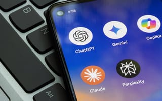 Smartphone screen displaying AI app icons: ChatGPT, Gemini, Copilot, Claude, and Perplexity. Background shows part of a laptop keyboard, suggesting technology use.