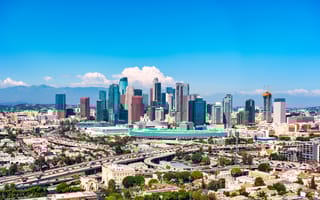 Skyline of a Los Angeles, California, under clear blue skies, featuring modern skyscrapers, highways, and mountains in the distance. A vibrant, urban atmosphere.