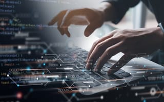 A close up of hands typing on a laptop keyboard with a transparent illustration of coding and connected data points overlaying the photo.