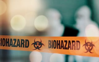 Orange tape featuring the word BIOHAZARD in front of a blurred image of two workers in white protective gear.