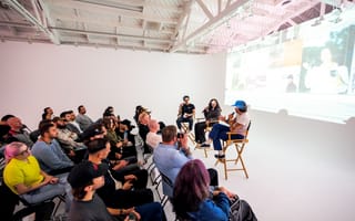A group attends a VSCO event in a white room with three speakers sitting on director's chairs in front of a projected screen.