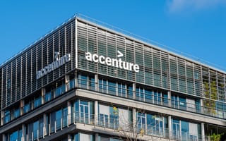 Modern building with "Accenture" logo in bold white letters on the facade. The structure features sleek glass panels and metal accents under a clear blue sky.