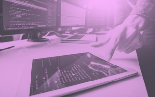 A person pointing to a tablet with code on it. There are screens in the background with code.