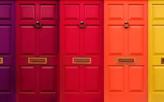 A row of brightly colored doors with door knockers.