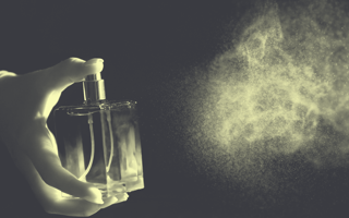 A hand sprays a bottle of perfume