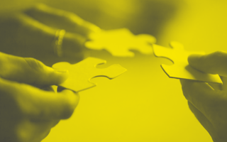 Closeup of hands showing people working together to combine puzzle pieces.