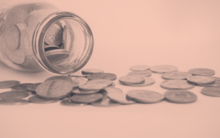 A glass jar of money that's been overturned, coins spilling out.