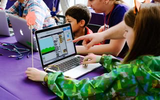 children sitting at laptops using learning applications with the help of adults standing over their shoulders
