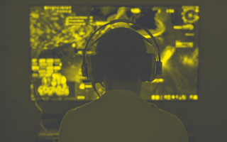 Person playing a video game, using headphones, image shot from behind.