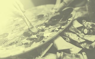Closeup of a person using a painter's palette. Pile of painting tubes in the background.