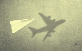 A paper plane in mid-air that has an airplane shadow.