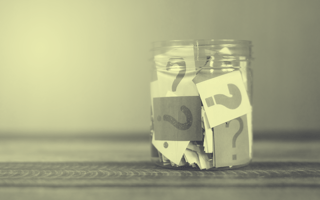 A glass jar filled with papers that have question marks on them.