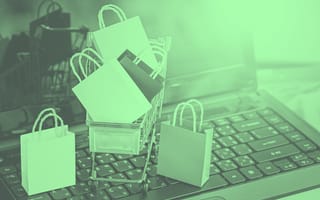 A miniature cart filled with shopping bags sitting on a laptop.