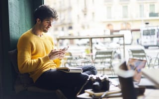 A man is sitting down looking at a smart phone.