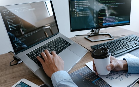 Man works on multiple computer displays while holding coffee cup