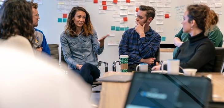Ontra coworkers having a team meeting in the office with post it notes on the wall in the background