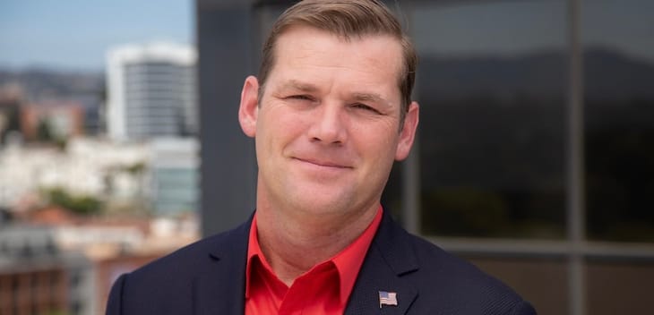 A man wears a red button up shirt and black blazer