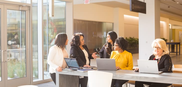 Five Liberty Mutual team members gather at a community table in Liberty Mutual’s common area with laptops, in discussion.