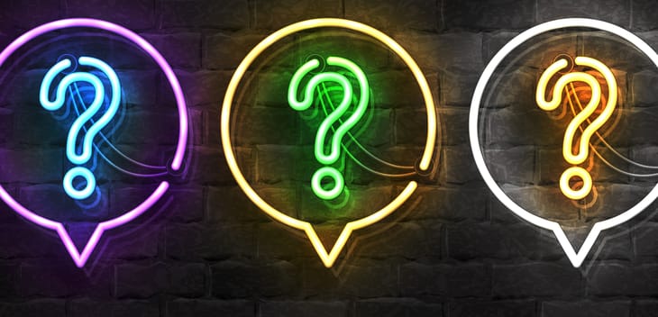 Image of brick wall with a row of three neon lights shaped like question marks within neon light speech bubbles