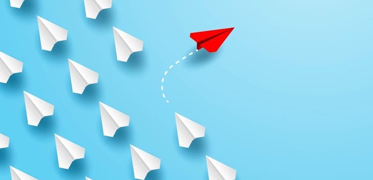 One red paper airplane changing direction from many white paper airplanes