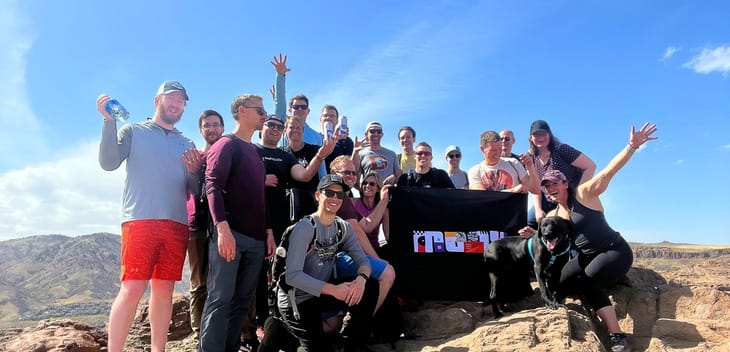 Moov employees hold a flag with the company logo on top of a mountain.