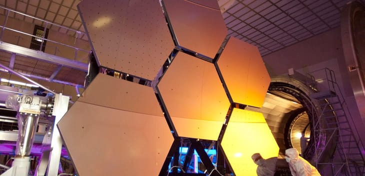 A scientist looking over several large, hexagonal panels of metal in a lab.